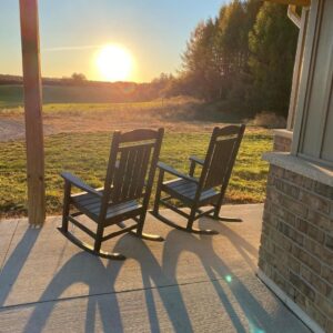 2 rocking chairs on a porch facing a field at sundown
